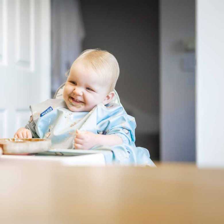 Baby Daphne is smiling as she sits in a high chair with a bib on. In the foreground is her mum Laura and the Alexa device BWBF gave them