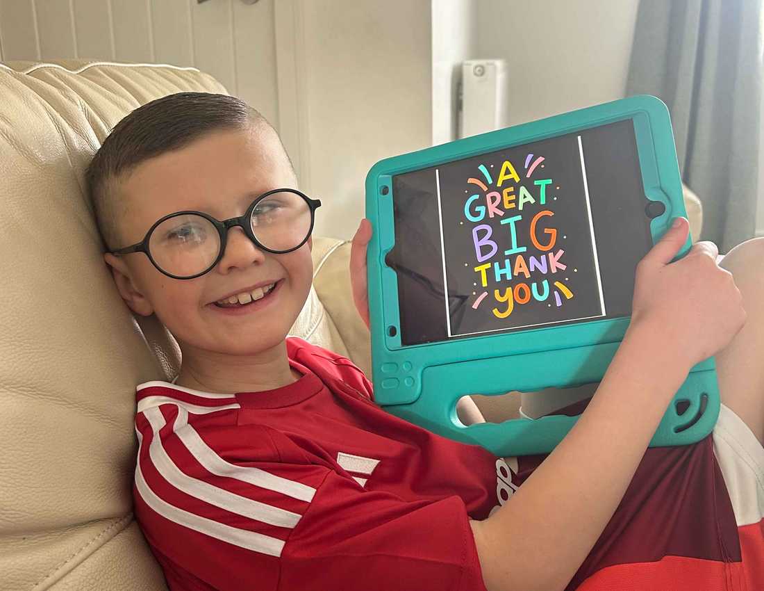 Nine year old Ryder smiles as he holds up his iPad from BWBF. On the screen, text reads 'a great big thank you'.
