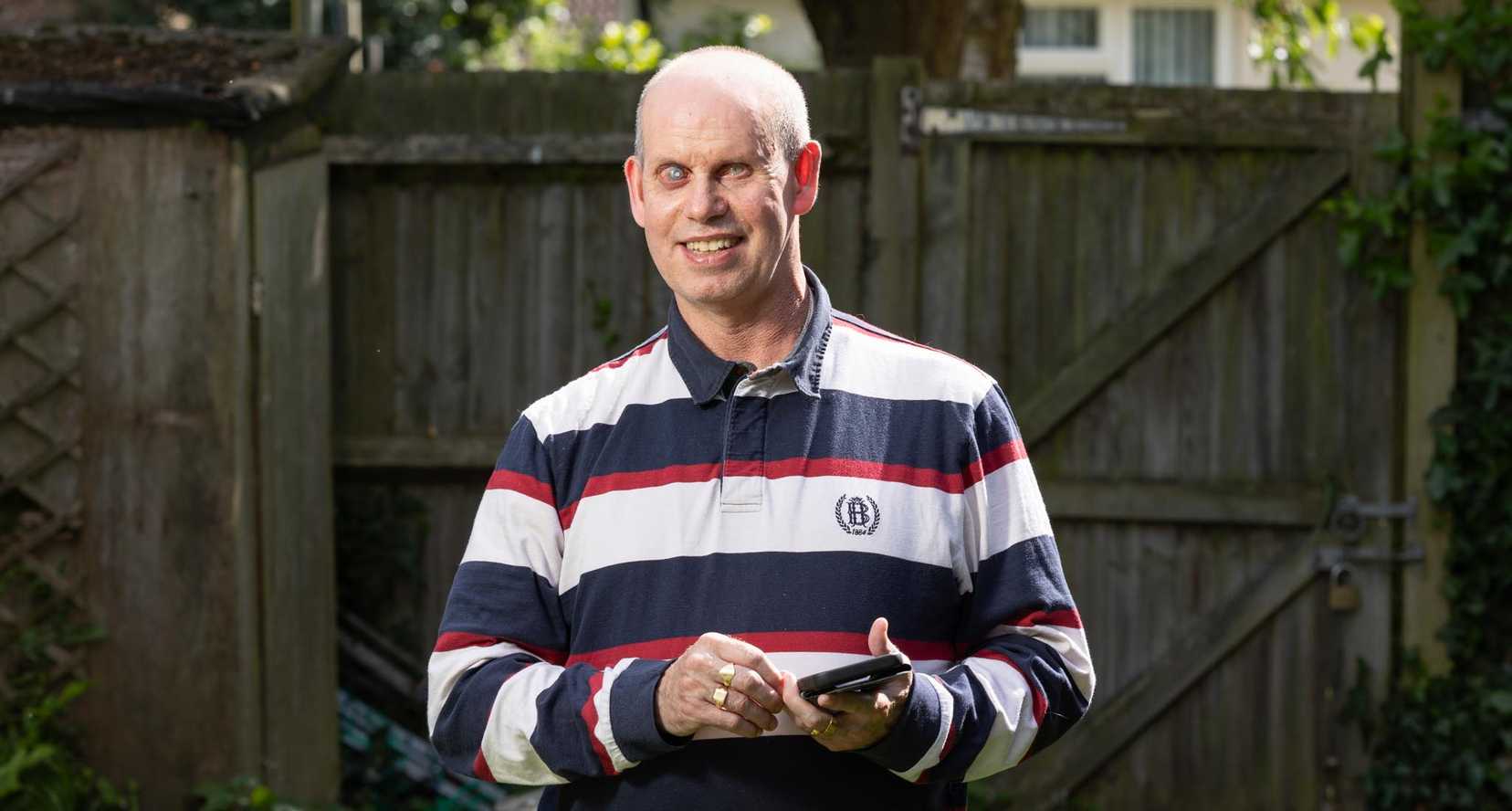 Brian, one of BWBF's app users, stands smiling in his garden as he holds his mobile phone.