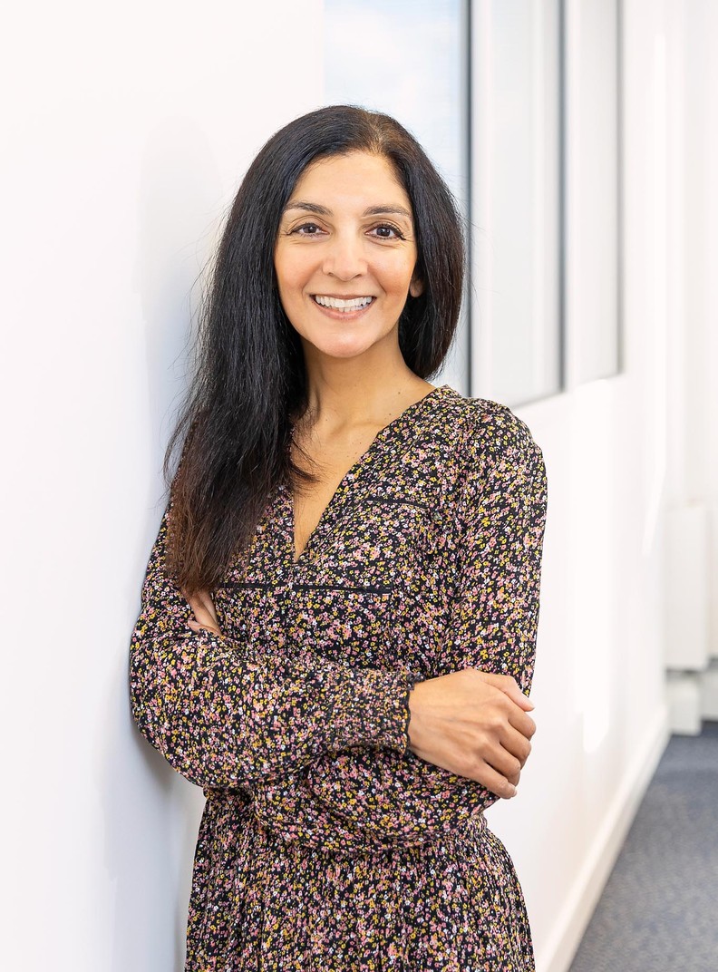 BWBF Communcations & Data Assistant Divya Kohli pictured in an office. She has her arms crossed and is smiling and wearing a brown floral dress.