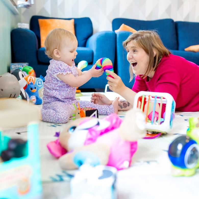 A mother and baby, laughing surrounded by toys in a room, playing on the floor