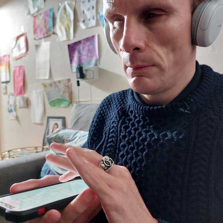 A man in a blue jumper, wearing headphones, uses a mobile phone