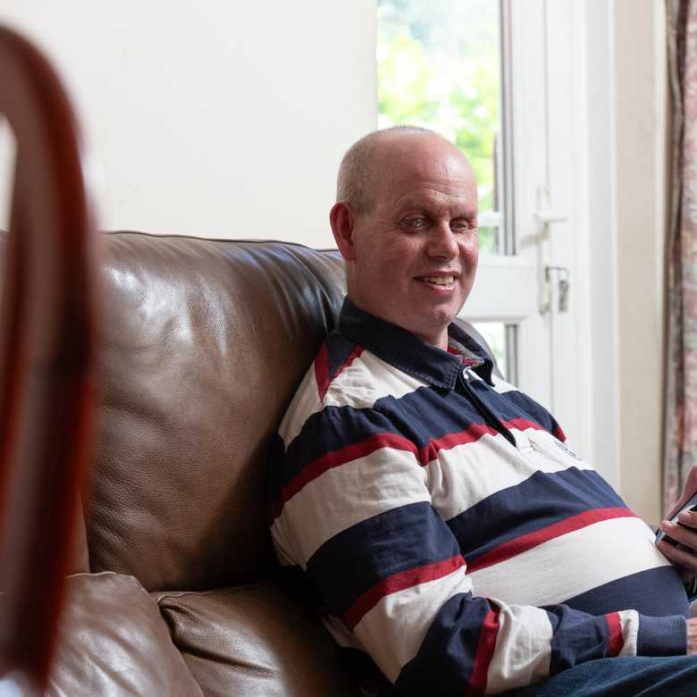 Brian sits on a brown leather sofa. He is smiling and his phone is in his hand