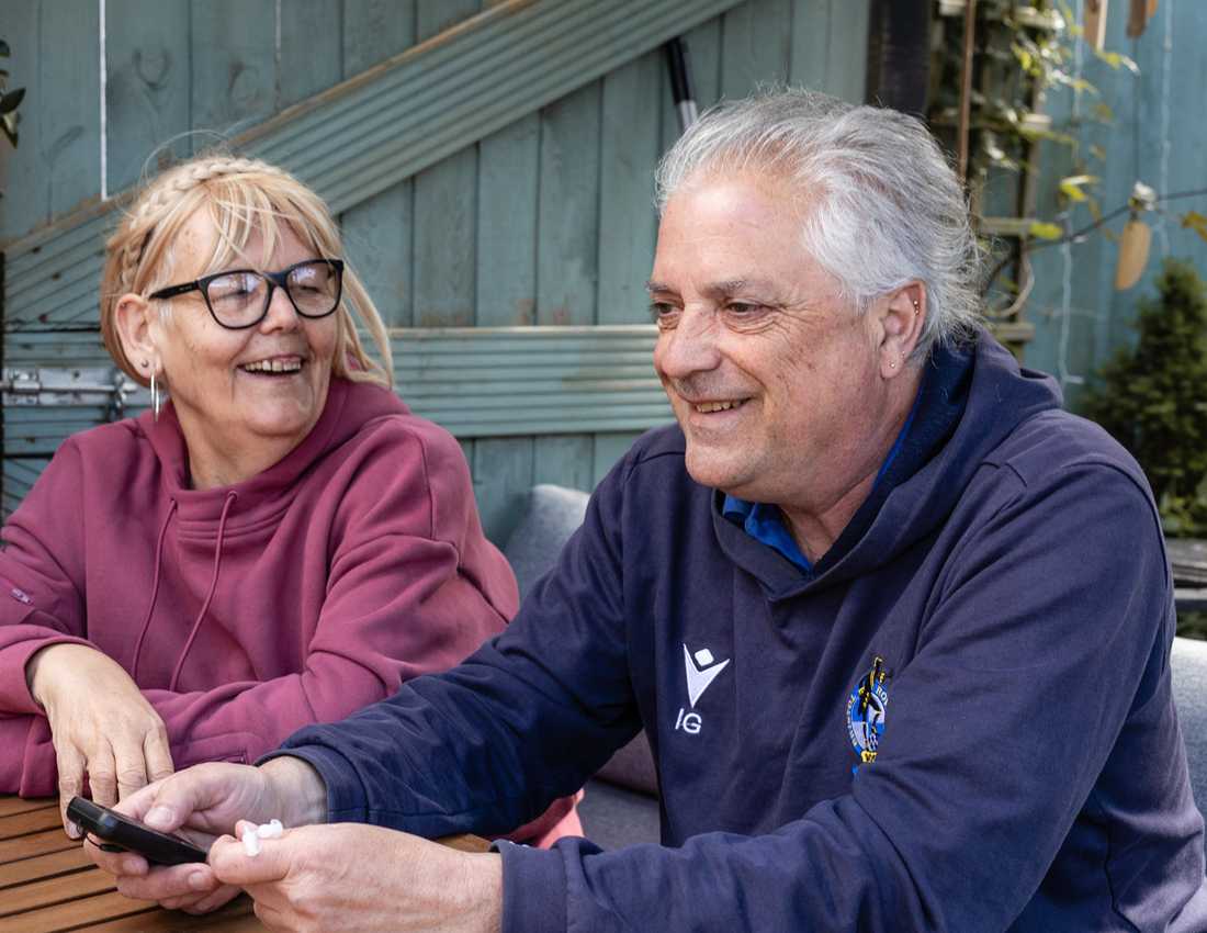 Ian sits smiling at a garden table wearing his favourite Bristol Rovers top. He's clutching the pocket radio Visably gave him as his wife Pat smiles at him lovingly.