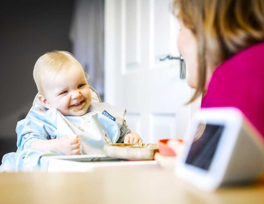 Mother and her baby in a highchair, both smiling with an Alexa screen on the table beside them