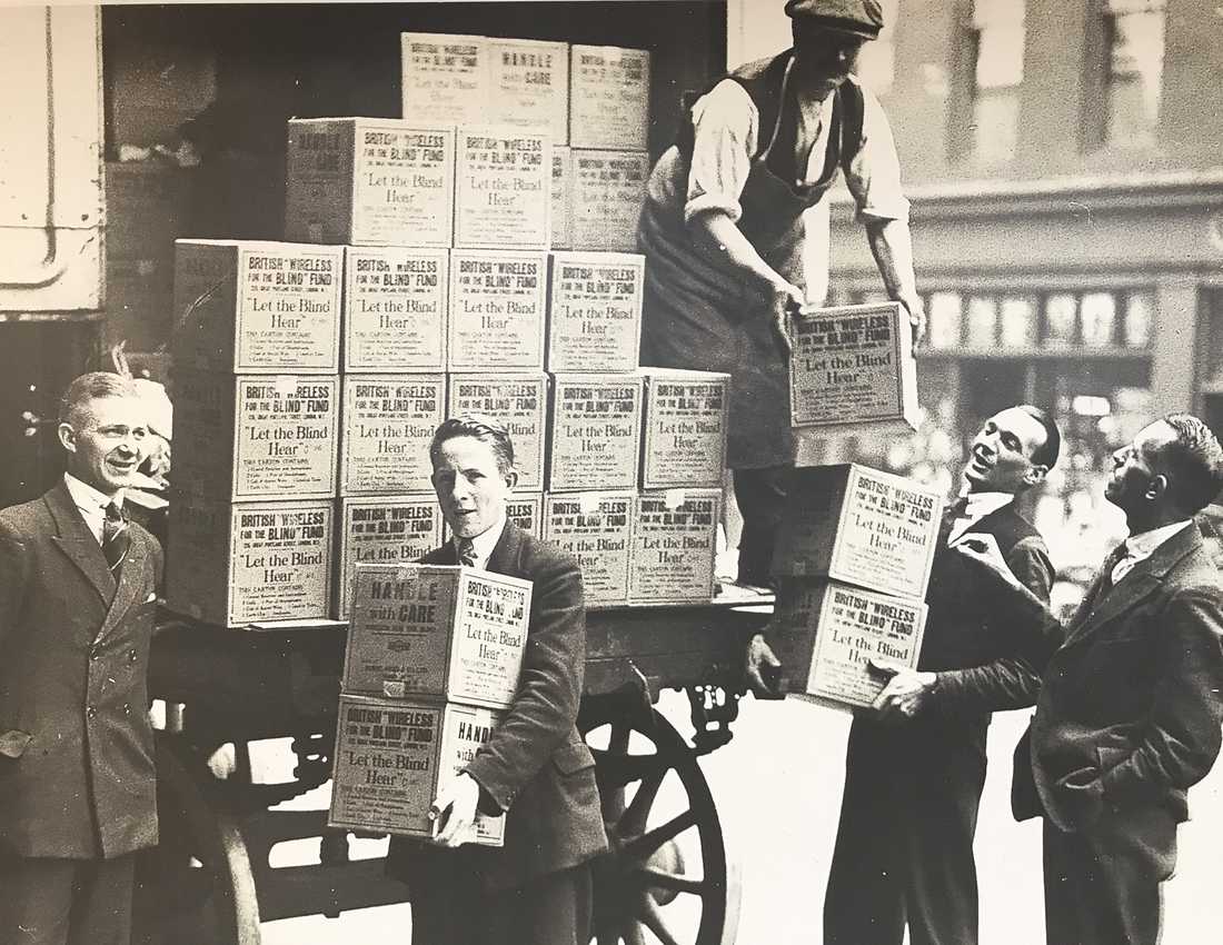 A sepia historical photo of young men unloading boxes labelled BWBF off a truck.